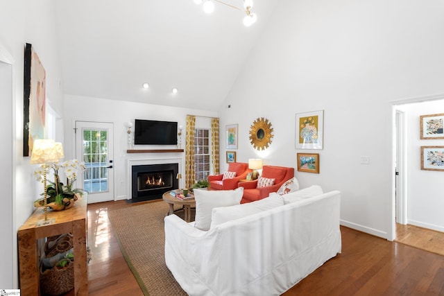 living room featuring a fireplace with flush hearth, high vaulted ceiling, baseboards, and wood finished floors