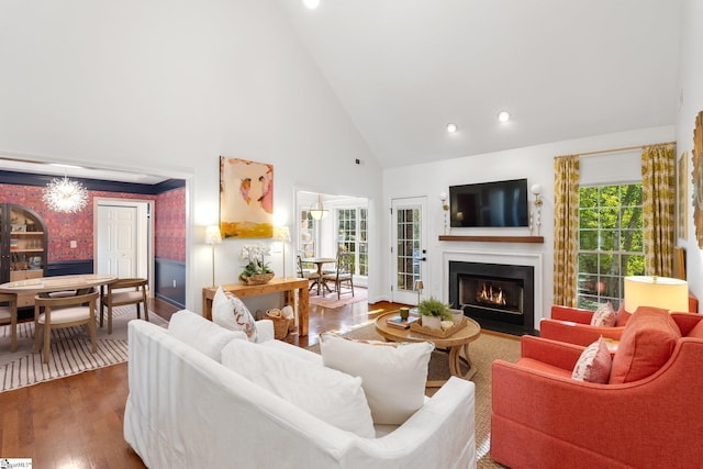 living room featuring a fireplace with flush hearth, high vaulted ceiling, hardwood / wood-style floors, wainscoting, and wallpapered walls