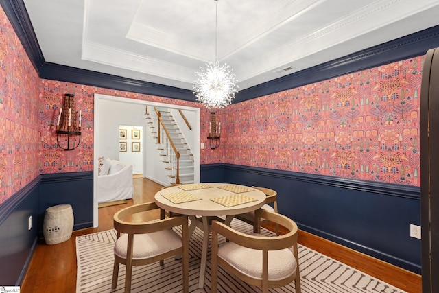 dining area featuring a wainscoted wall, a tray ceiling, wood finished floors, stairway, and wallpapered walls