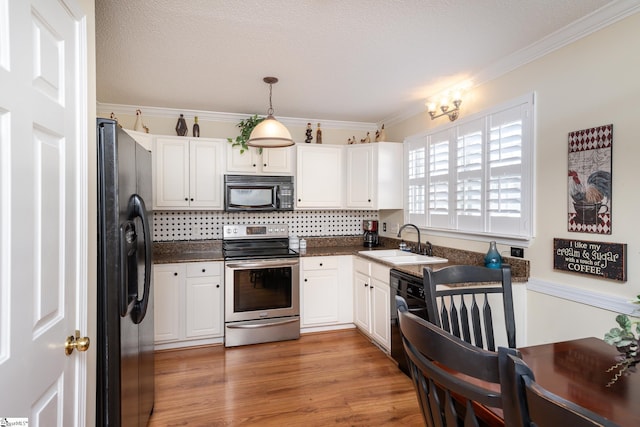 kitchen with black appliances, ornamental molding, a sink, dark countertops, and light wood finished floors