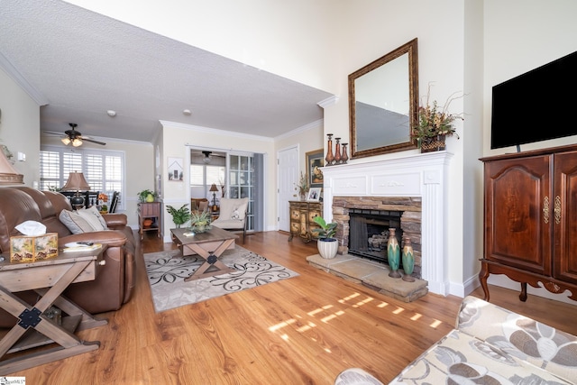 living room with a textured ceiling, wood finished floors, a fireplace, crown molding, and ceiling fan