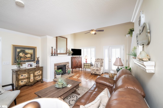 living room with ceiling fan, a textured ceiling, a stone fireplace, and wood finished floors