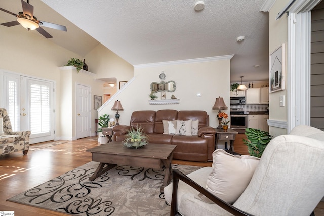 living room with light wood-style flooring, a ceiling fan, ornamental molding, a textured ceiling, and vaulted ceiling