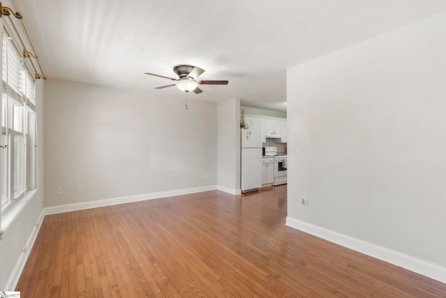 spare room featuring light wood finished floors, a ceiling fan, and baseboards