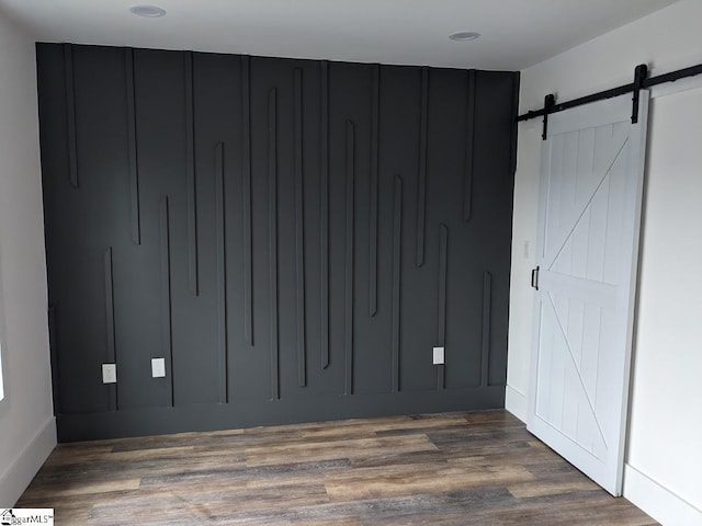 unfurnished bedroom featuring a barn door, wood finished floors, and a decorative wall