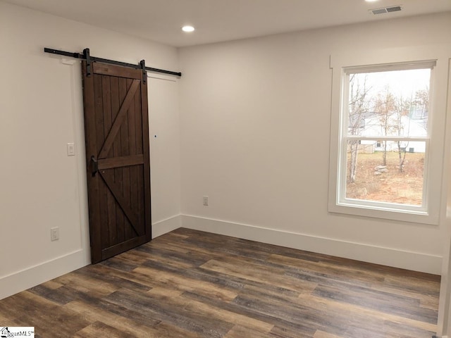 unfurnished room featuring a barn door, plenty of natural light, visible vents, and dark wood-style flooring