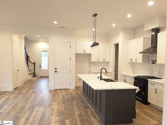 kitchen with black gas range oven, dark wood finished floors, a sink, white cabinets, and wall chimney range hood