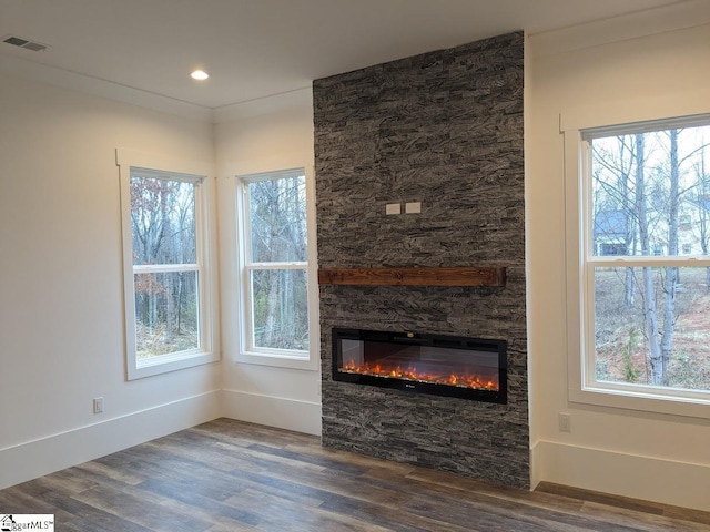 unfurnished living room featuring a stone fireplace, wood finished floors, visible vents, and baseboards