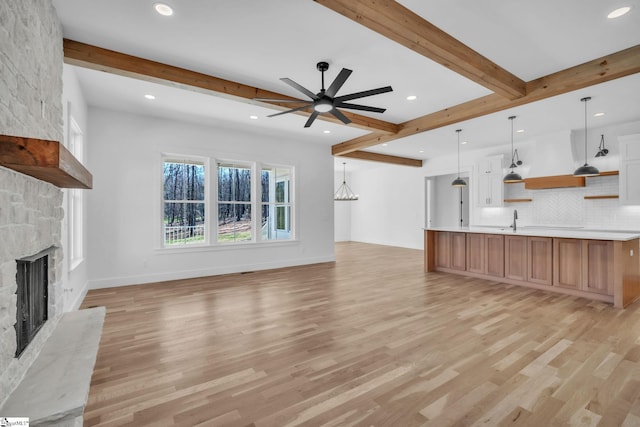 unfurnished living room featuring a sink, beam ceiling, light wood-style floors, and a fireplace