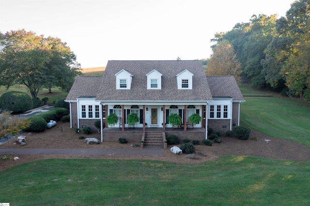 new england style home featuring brick siding, a front yard, roof with shingles, covered porch, and crawl space