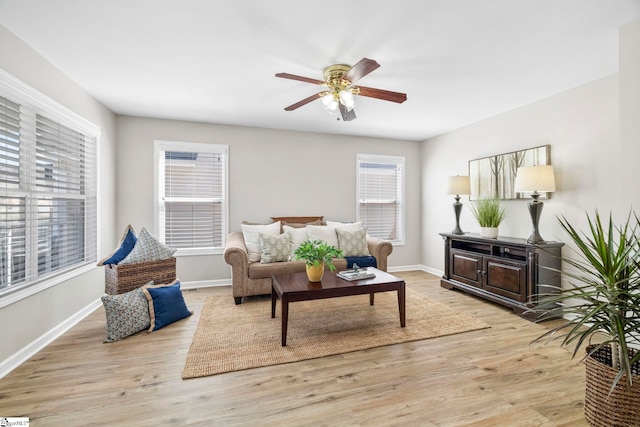 living room featuring a ceiling fan, baseboards, and light wood finished floors