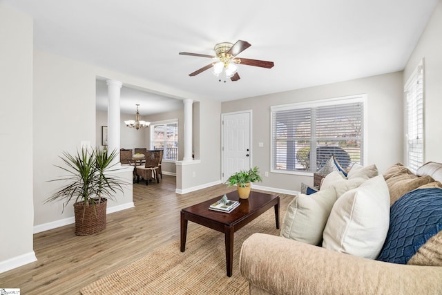 living room featuring ceiling fan with notable chandelier, baseboards, light wood-type flooring, and ornate columns