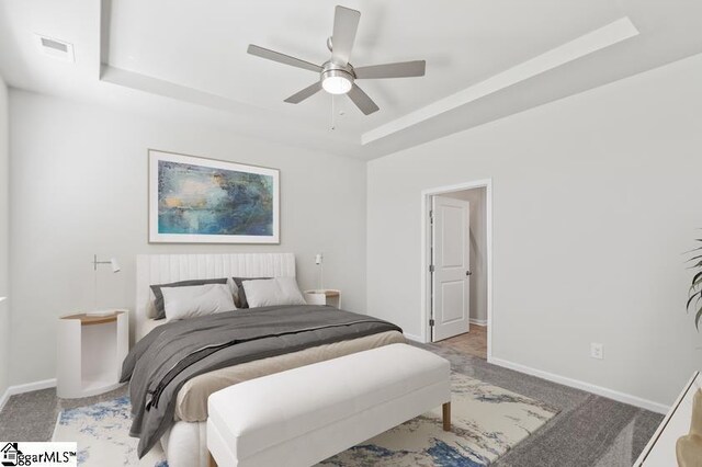 carpeted bedroom with ceiling fan, a raised ceiling, and baseboards