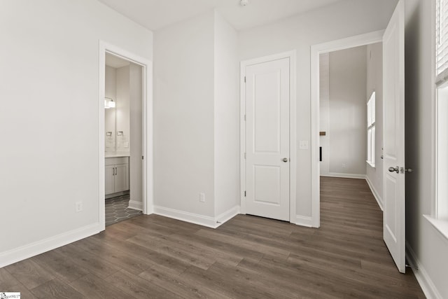 unfurnished bedroom with ensuite bath, dark wood-type flooring, and baseboards