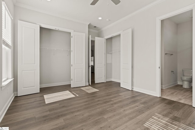 unfurnished bedroom featuring baseboards, crown molding, multiple closets, and wood finished floors