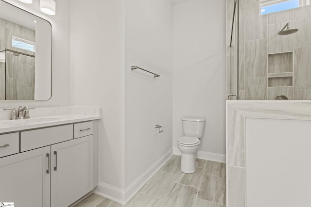 full bath featuring baseboards, tiled shower, toilet, and vanity