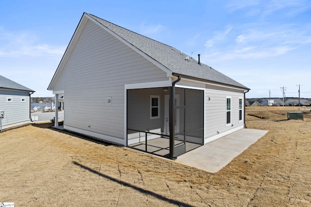 rear view of property with a shingled roof, a patio, and a sunroom