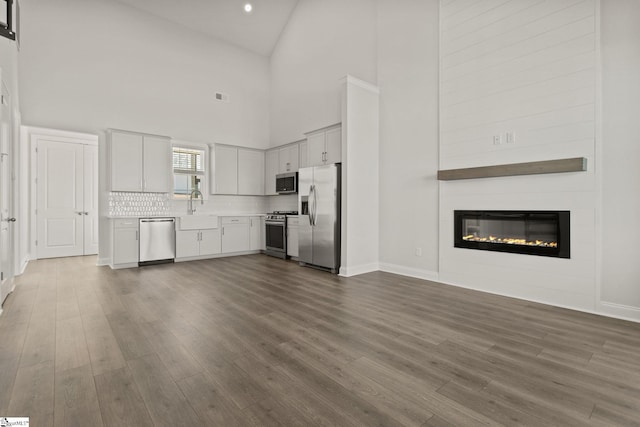 unfurnished living room with dark wood-style floors, visible vents, a fireplace, a sink, and vaulted ceiling