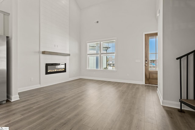 unfurnished living room with dark wood finished floors, visible vents, a large fireplace, and baseboards