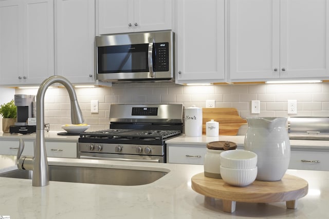 kitchen with backsplash, white cabinets, stainless steel appliances, and a sink