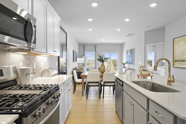 kitchen with visible vents, light wood-style flooring, a sink, backsplash, and stainless steel appliances