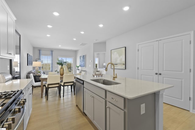 kitchen with light wood finished floors, gray cabinets, a sink, appliances with stainless steel finishes, and open floor plan