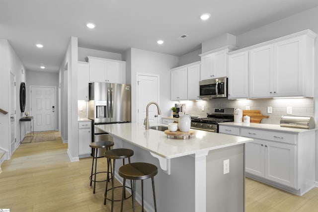 kitchen with a center island with sink, recessed lighting, a sink, light wood-style floors, and appliances with stainless steel finishes