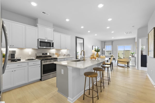 kitchen featuring visible vents, a kitchen island with sink, a sink, backsplash, and appliances with stainless steel finishes