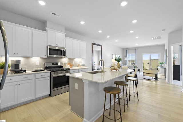 kitchen featuring a sink, visible vents, appliances with stainless steel finishes, and a center island with sink