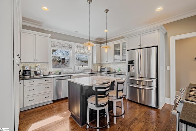 kitchen featuring dark wood-style floors, appliances with stainless steel finishes, a breakfast bar area, crown molding, and hanging light fixtures