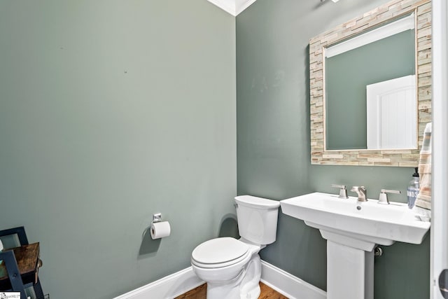 half bath with toilet, baseboards, and wood finished floors