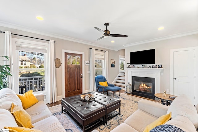 living area with a glass covered fireplace, stairs, crown molding, and wood finished floors