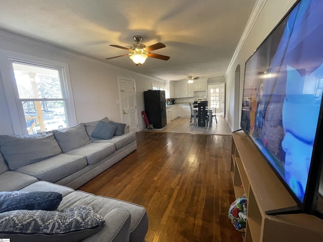 living room featuring light wood-style flooring, a textured ceiling, ornamental molding, and a ceiling fan