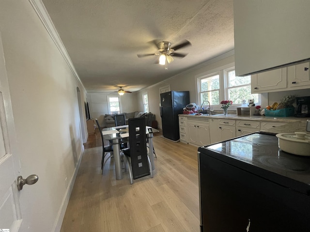 kitchen featuring crown molding, light wood-style floors, white cabinets, black appliances, and a sink