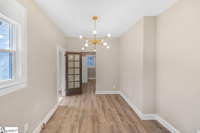 unfurnished dining area with wood finished floors, baseboards, and a chandelier