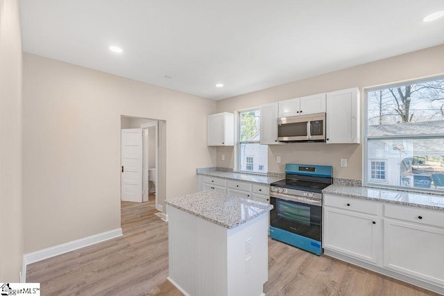 kitchen with baseboards, light stone countertops, appliances with stainless steel finishes, light wood-style floors, and white cabinets