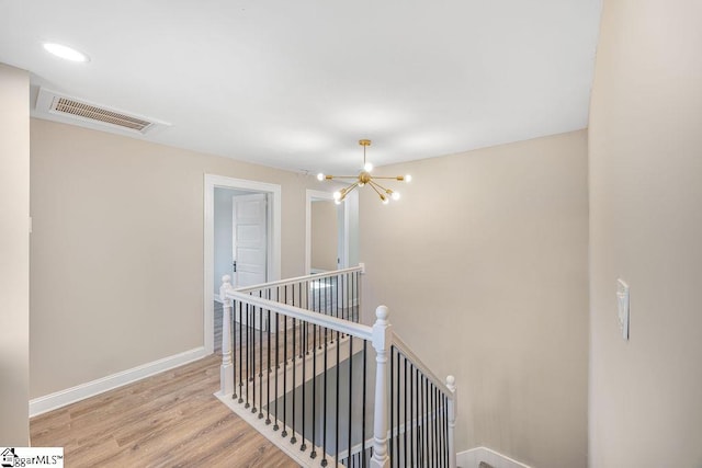 corridor featuring wood finished floors, visible vents, baseboards, a notable chandelier, and an upstairs landing