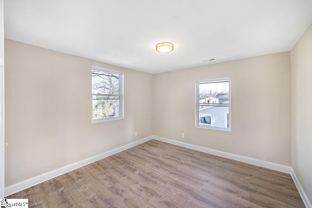 empty room featuring visible vents, wood finished floors, and baseboards