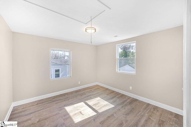 empty room with a wealth of natural light, attic access, and wood finished floors