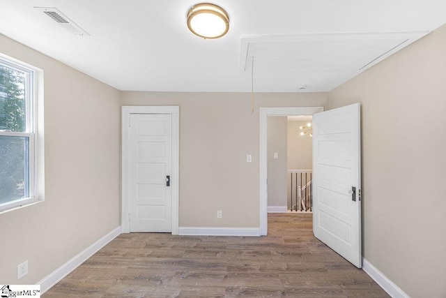 unfurnished bedroom featuring visible vents, baseboards, attic access, and wood finished floors