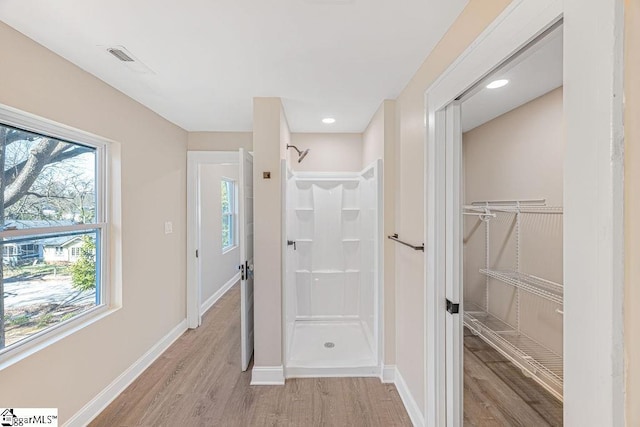 full bath featuring a spacious closet, wood finished floors, baseboards, and walk in shower