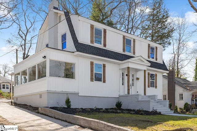 view of front of house featuring a sunroom, a gambrel roof, roof with shingles, and a chimney