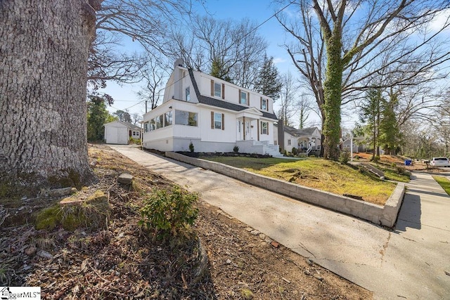 colonial inspired home with a shingled roof, a gambrel roof, a chimney, an outdoor structure, and a storage unit