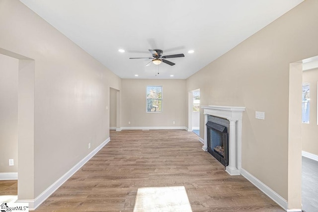 unfurnished living room featuring light wood finished floors, ceiling fan, a fireplace, and baseboards