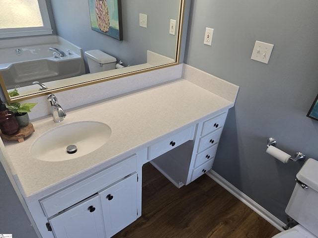 bathroom with baseboards, toilet, a garden tub, wood finished floors, and vanity