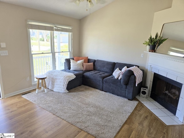 living area with a fireplace with flush hearth, wood finished floors, and ceiling fan