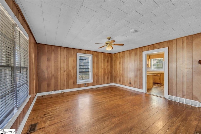 spare room with visible vents, wood walls, ceiling fan, and wood-type flooring