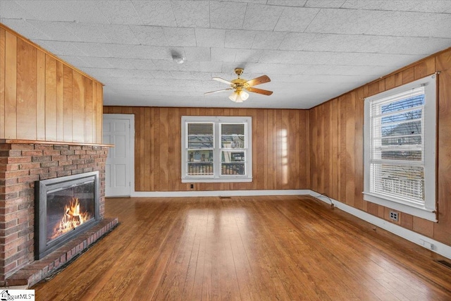 unfurnished living room featuring a brick fireplace, baseboards, wood-type flooring, and wood walls