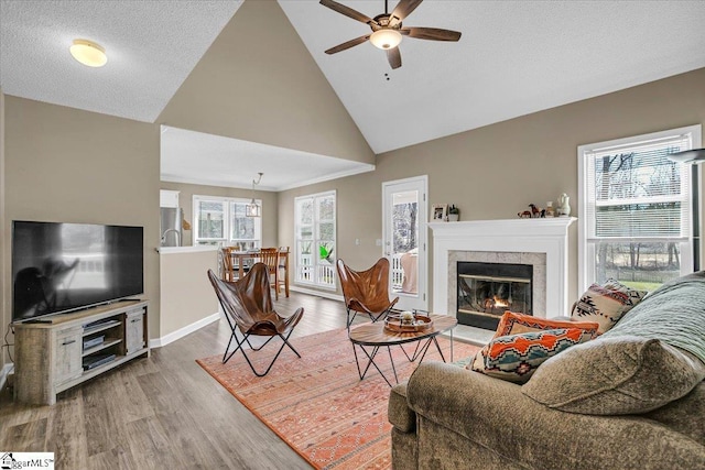 living room featuring baseboards, ceiling fan, wood finished floors, a glass covered fireplace, and high vaulted ceiling