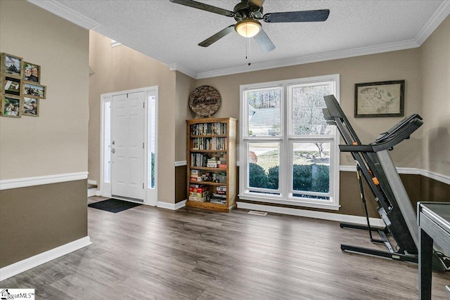 workout area with a textured ceiling, wood finished floors, baseboards, and ornamental molding